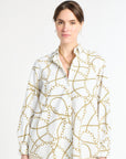 Woman modeling white and gold patterned top against a white background