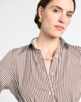 Woman wearing a brown and white striped shirt with a pearl necklace against a white background