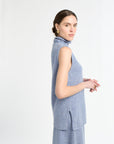 Woman with blue sleeveless knit on with white background.