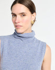 Woman with blue sleeveless knit on with white background.