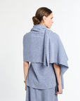 Woman wearing a light blue poncho over a dress on a white background
