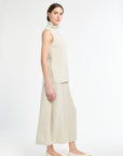 Woman wearing a beige sleeveless top and high-waisted pants on a white background