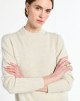 Woman wearing a cream sweater with arms crossed on a white background