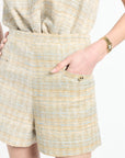 Golden and light blue tweed shorts on white background with a woman's hand in the pockets