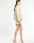 Side angle shot of woman wearing a gold and light blue blazer and shorts set on a white background