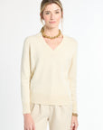 Woman wearing a light-colored sweater and pants with a gold necklace on a white background