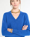 Woman wearing a blue sweater with gold jewelry on a white background