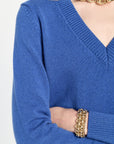 Blue sweater worn by a person with gold jewelry on a white background