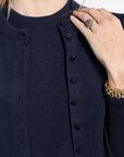 Navy blue cardigan with black buttons worn by a person, with a hand touching the fabric.