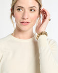 Woman wearing a cream sweater with a gold bracelet on a white background