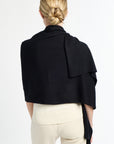 Person wearing a black drapey top over a white outfit on a plain background