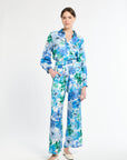 Woman wearing a tucked in blue and green floral shirt with matching pants on a white background