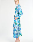 Side profile of woman wearing silk shirt dress with blue and green floral pattern on a white background