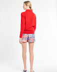 Woman wearing a red sweater and colorful shorts on a white background