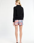 Woman wearing a black sweater and colorful floral shorts on a white background