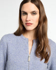 Woman wearing a light blue zip-up sweater against a white background