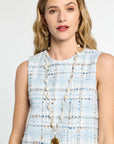 Woman wearing a light blue tweed dress with a long pearl necklace against a white background