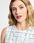 Woman wearing a light blue textured dress with a pearl necklace against a white background