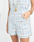 Person wearing a light blue tweed romper with gold buttons on a white background