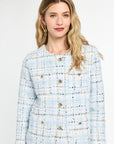 Woman wearing a light blue tweed suit with gold buttons on a white background