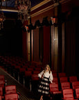 Woman standing in a dimly lit theater with red seats and a chandelier.