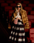 Woman in a fur coat and plaid skirt holding popcorn in a movie theater.