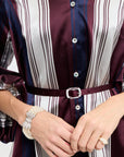 Close-up of a person wearing a striped dress with a belt, hands adjusting it, and accessories.