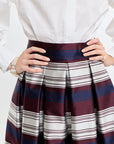 Person wearing a white shirt and a striped skirt with hands on waist against a white background
