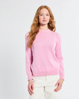 Woman wearing a pink sweater and white pants against a light gray background
