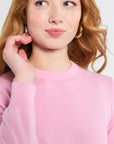 Woman modeling a pink sweater wearing gold hoops against a white background