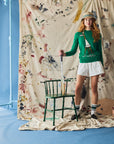 Person wearing a long sleeve green sweater with a giraffe against a blue painted backdrop