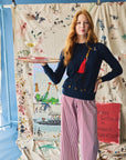 Woman holding a tray with a drink, wearing a navy sweater with a giraffe on it, standing in front of a colorful backdrop