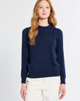 Woman wearing a navy sweater and white pants on a light gray background