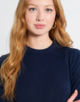 Woman with red hair wearing a navy blue sweater against a white background