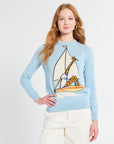 Woman wearing a light blue sweater with a giraffe and sailboat design on a white background