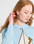 Woman wearing a light blue sweater with a sailboat and giraffe design on a white backdrop