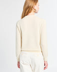 Woman wearing a light-colored sweater and white pants on a plain background