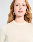 Woman wearing a long sleeve cream cashmere sweater on a white backdrop