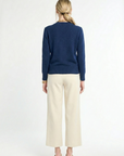 back of woman wearing navy v-neck sweater and cream pants on a white background