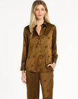 A woman modeling the Golden Umber Eleanor Shirt with coordinating Diane Pants, front view with one hand in a pocket, photographed against a plain white studio background.