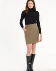 A woman modeling the Painter's Fleck Herringbone Meg Mini Skirt with a black turtleneck and knee-high boots, front view, photographed against a plain white studio background.