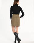 A woman modeling the Painter's Fleck Herringbone Meg Mini Skirt with a black turtleneck and knee-high boots, back view, photographed against a plain white studio background.