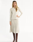 A woman modeling the cream side of the Chestnut Windowpane Plaid Reversible Crewneck with the matching flared skirt and brown boots, front view, photographed against a plain white studio background.