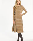 A woman modeling the chestnut side of the Windowpane Plaid Reversible Crewneck with the matching skirt and brown boots, front view, photographed against a plain white studio background.