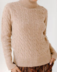 A person wearing a beige cable knit turtleneck sweater.