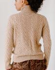 Back view of model wearing the Camel Cable-Knit Turtleneck sweater paired with paisley patterned pants, showcasing the sweater's texture.