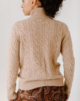 Back view of model wearing the Camel Cable-Knit Turtleneck sweater paired with paisley patterned pants, showcasing the sweater's texture.