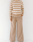 Model wearing the camel/cream Classic Striped Cashmere Crew, paired with wide-leg camel trousers and beige flats, on a white background.