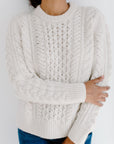 Model wearing the Cream chunky Aran cable knit Fisherman Crewneck sweater, paired with jeans in front of a white background.