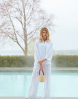 Woman in a white outfit standing by a pool with bare feet.